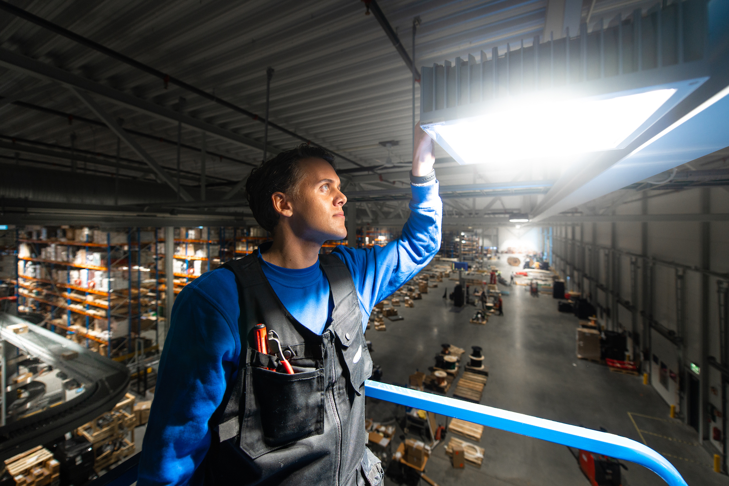 Elektriker monterer lys i taket av industrielt lagerbygg