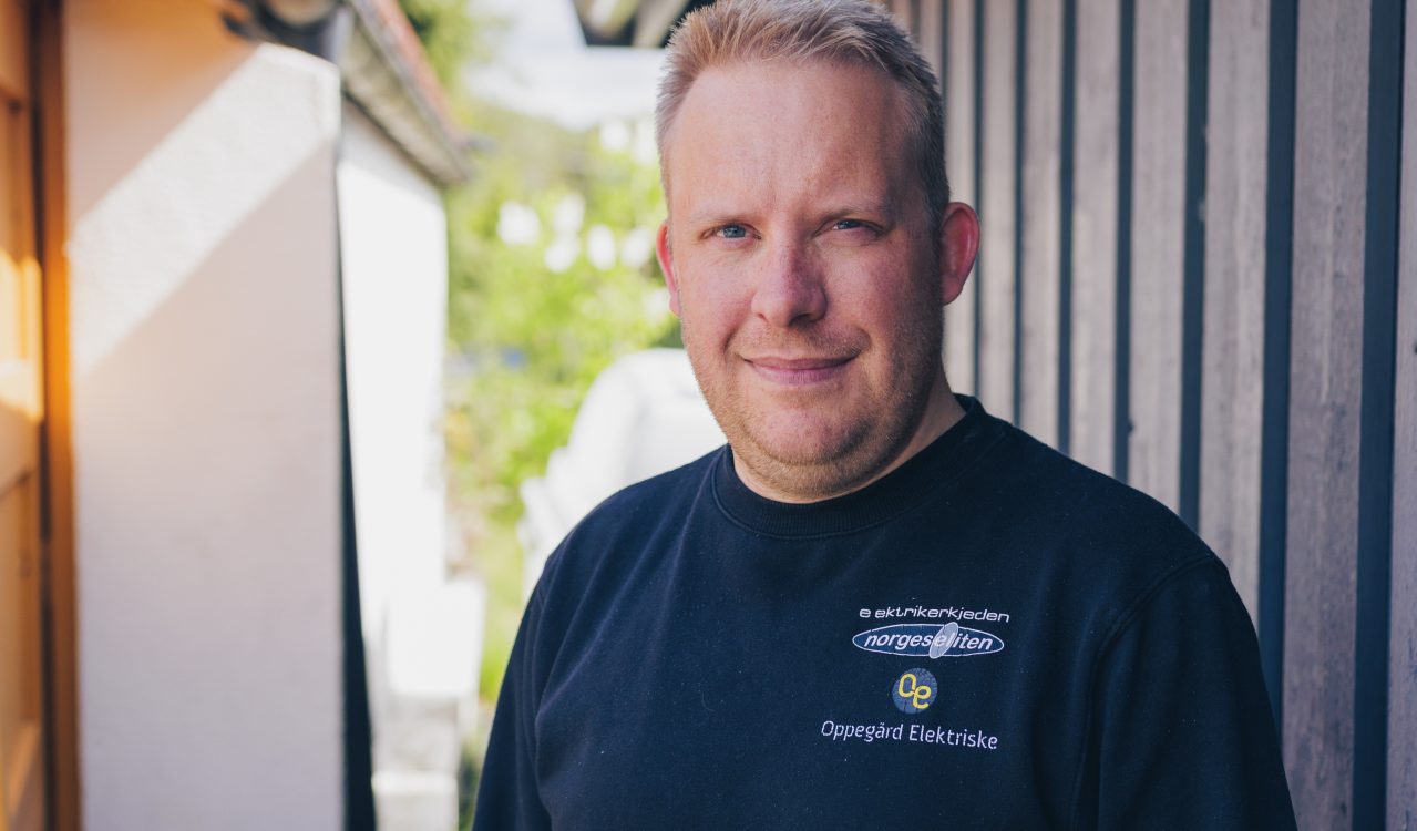 Elektriker Anders Bakke foran husvegg ikledd arbeidsgenser med logo.