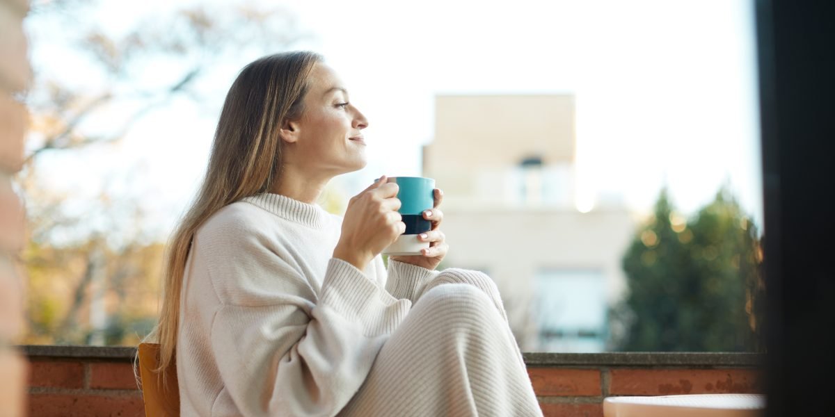 Kvinne som slapper av og drikker te og nyter utsikten ved stort vindu.