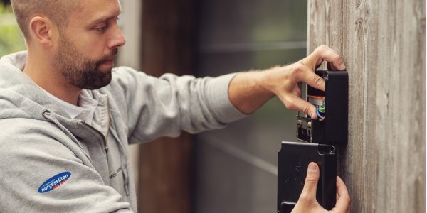 ung elektriker med grå genser monterer veggfeste til elbillader på brun husvegg